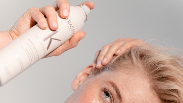 A Woman spraying dry shampoo into her hair.