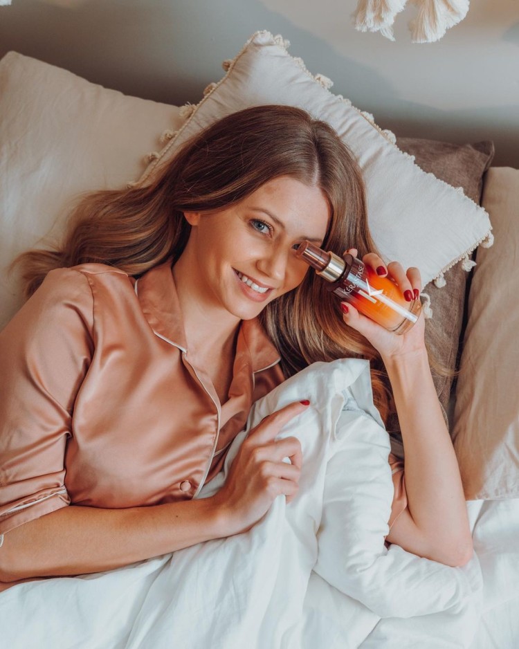 A woman in bed holding a Kerastase bottle.